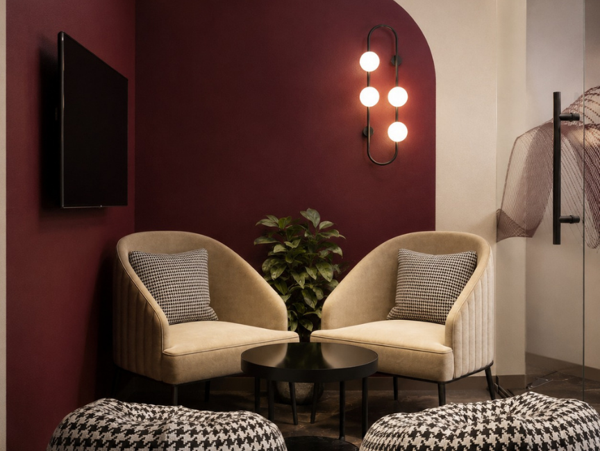 Maroon accent lounge nook with beige velvet chairs, houndstooth pillows, and a bubble wall sconce